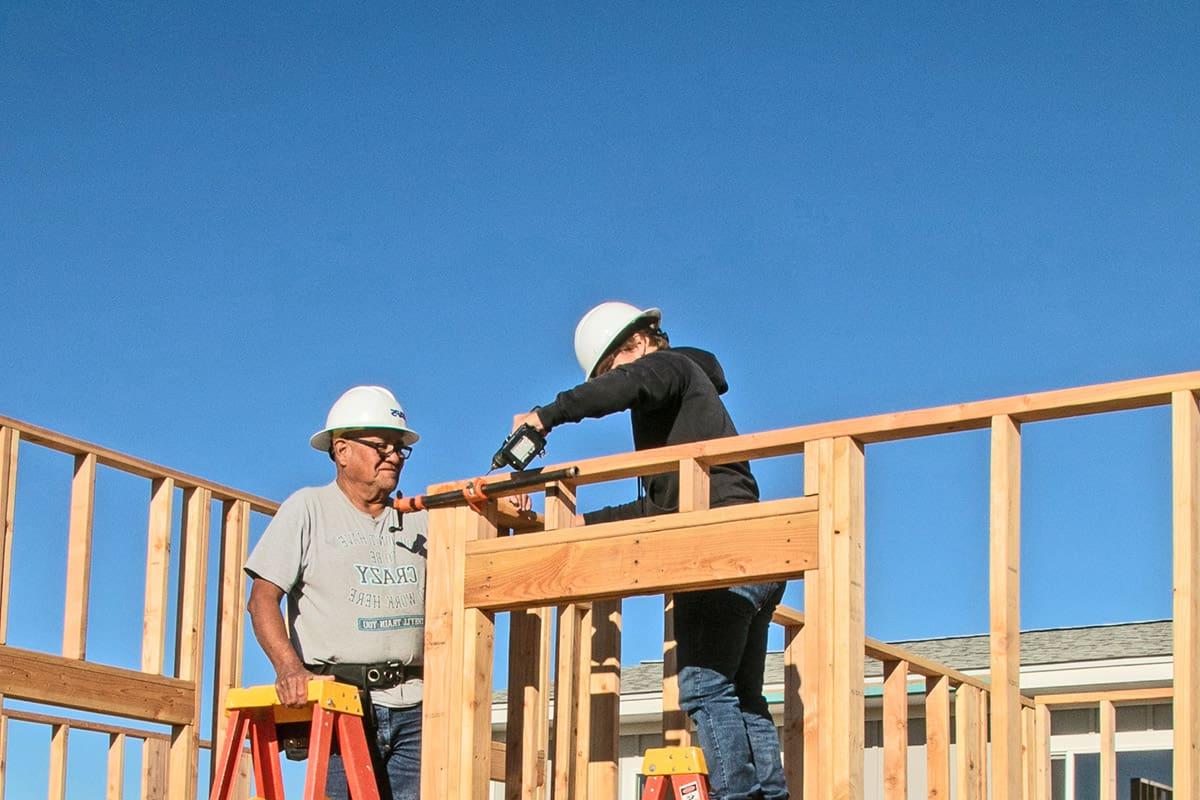 intern on a construction job site receives instruction from mentor on house framing.